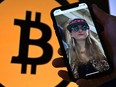 This illustration photo shows Heather Morgan, also known as "Razzlekhan," on a phone in front of the Bitcoin logo displayed on a screen, in Washington, DC, February 9, 2022.