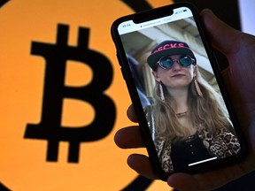 This illustration photo shows Heather Morgan, also known as "Razzlekhan," on a phone in front of the Bitcoin logo displayed on a screen, in Washington, DC, February 9, 2022.