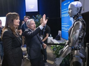 Federal Industry Minister Francois-Philippe Champagne says hello to an AI robot as Helene Desmarais, executive chairwoman, of IVADO Labs looks on at the All In artificial intelligence conference Wednesday, September 27, 2023 in Montreal.