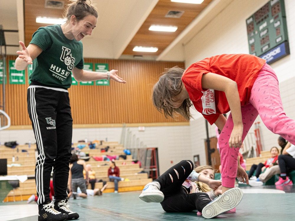 La luchadora de la U of S, Katie Dutchak, presenta el deporte de la lucha libre a los estudiantes de cuarto grado Aaliyah Carter-Pederson (centro) y Zayda Primeau (derecha) del Centro de Educación y Bienestar St. Mary's durante el primer Festival anual de lucha libre en memoria de Natasha Fox en la Universidad de Saskatchewan. Gimnasio educativo en Saskatoon el viernes 24 de noviembre de 2023.