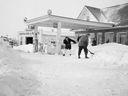 A photo of people clearing snow at a service station after the heaviest snowfall of the season, from March 14, 1955. People around town were clearing snow in the early hours and the city was using all the equipment it had to clear the streets.