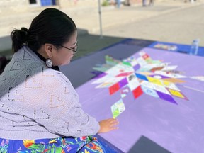 カミシャ・アレクソンさんは、2024年8月31日にサスカチュワン州サスカトゥーンで行われた薬物過剰摂取啓発デーの集会で、記念の星型ブランケットにタイルを置いている。