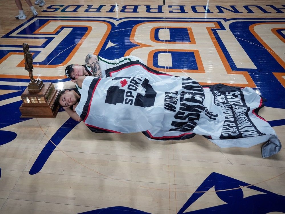 University of Saskatchewan Huskies' Maya Flindall, front, and Tea DeMong lie on the court under the championship banner and beside the trophy after defeating the Carleton Ravens in the U Sports women's national basketball championship final, in Vancouver, on Sunday, March 16, 2025.