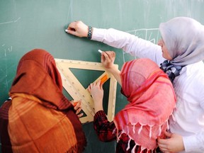 In this stock photo, a Muslim teacher works with students wearing hijabs on a chalkboard.