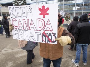 A man hides his face while promoting his anti-Motion 103 sign outside City Hall in Calgary on March 4, 2017. (Lyle Aspinall/Postmedia Network)