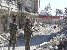 In this picture taken on Monday Oct. 16, 2017 and provided by The Syrian Democratic Forces (SDF), a U.S.-backed Syrian Kurdish forces outlet that is consistent with independent AP reporting, shows Syrian Democratic Forces (SDF) fighters, stand on destroyed street where they battle against the Islamic State militants, in Raqqa, Syria. (Syrian Democratic Forces via AP)