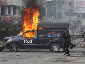 A Pakistani police officer aims his gun towards the protesters next to a burning police vehicle during a clash in Islamabad, Pakistan, Saturday, Nov. 25, 2017.