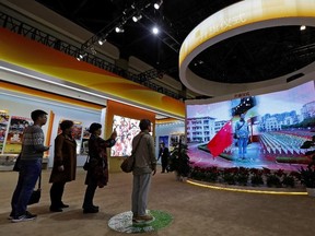 In this Oct. 23, 2017, file photo, visitors watch a man appearing on a screen as he experiences a national anthem flag raising ceremony at an exhibition highlighting China's achievements at the Beijing Exhibition Hall in the capital city where the 19th Party Congress is held in Beijing. (Andy Wong/AP Photo/Files)