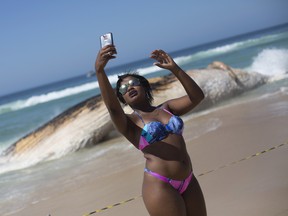 A woman poses for a selfie backdropped by the carcass of a humpback whale on Ipanema beach, in Rio de Janeiro, Brazil, Wednesday, Nov. 15, 2017. Biologist Rafael Carvalho said the whale appears to have been dead for a few days. Authorities were urging beachgoers who had flocked to Ipanema on a national holiday to stay away from the animal. (AP Photo/Silvia Izquierdo)