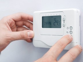 In this stock image, a man adjusts a wall-mounted thermostat.