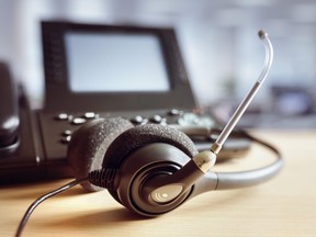 This stock photo shows a call centre headset sitting on an office desk next to a work phone.