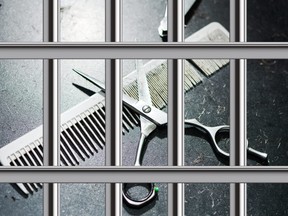 In this stock photo, a comb and scissors sit on a table at a barber behind prison bars.