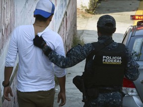 A federal police officer detains a man after a shootout broke out between police and gunmen on a central avenue in downtown Acapulco, Sunday, Nov. 12, 2017.