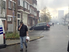 A man covers his face from smoke as he walks near the burning Milcamps waffle factory in Brussels, Thursday, Nov. 23, 2017.