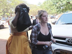 U.S. Citizen Martha O' Donovan, right, appears at the Harare Magistrates court escorted by a plain clothes police officer shielding her face in Harare, Saturday, November, 4, 2017. Police arrested and charged Donavan with subversion for allegedly insulting President Robert Mugabe on Twitter as a "sick man," lawyers said Friday. The offense carries up to 20 years in prison. (AP Photo/Tsvangirayi Mukwazhi)