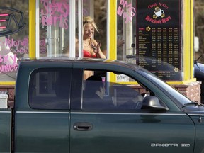 In this Feb. 2, 2010, file photo, a barista at a Grab-N-Go Bikini Hut espresso stand holds money as she waves to a customer, just outside the city limits of Everett, Wash., in Snohomish County. Seven bikini baristas and the owner of a chain of the coffee stands called "Hillbilly Hotties" sued the city of Everett, Washington, on Monday, Sept. 11, 2017, saying two recently passed ordinances banning bare skin violate their right to free expression. The proprietor of another chain, the Grab-N-Go espresso huts, was convicted of sexual exploitation of a minor after he employed a 16-year-old girl at his stands. Prosecutors said his business model relied on the baristas performing lewd shows.