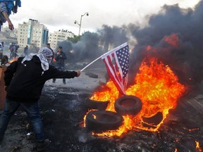 A Palestinian protester sets alight an America flag during clashes with Israeli troops at a protest against US President Donald Trump's decision to recognize Jerusalem as the capital of Israel, near the West Bank city of Ramallah on December 7, 2017.