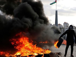 A Palestinian protester burns tyres during clashes with Israeli troops following a protest against US President Donald Trump's decision to recognize Jerusalem as the capital of Israel, near the Jewish settlement of Beit El, near the West Bank city of Ramallah, on December 7, 2017.