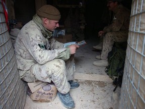 A soldier from A-Company 2 PPCLI sits near the entrance of his bunker to get enough light to catch up on some reading on Christmas morning. The troops are on a constant cycle of shifts manning a fighting position to protect their base, living in the bunker keeps them close to their position in the event of an attack.
