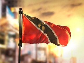 Trinidad and Tobago Flag Against City Blurred Background At Sunrise Backlight