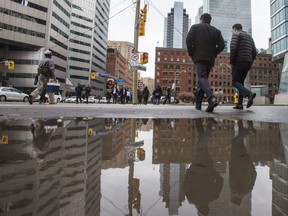 Pedestrians walk past a puddle on University Ave and Front St. W. on a warm day in downtown Toronto, Ont. on Thursday January 11, 2018.