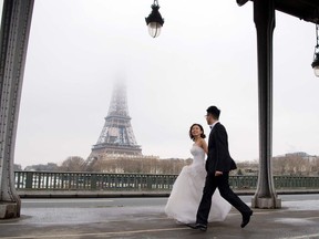 A couple in wedding dress and gown walks on the Pont de Bir-Hakeim bridge, with the Eiffel Tower in the background, on Valentine's Day, February 14, 2018 in Paris.