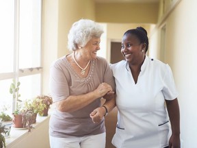 Portrait of smiling home caregiver and senior woman walking together through a corridor.