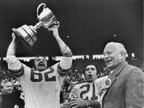 Moe Racine hoists the 1973 Grey Cup as teammate Wayne Giardino and former governor general Roland Michener look on.