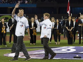 Former Toronto Blue Jays pitcher Roy Halladay's two sons, Ryan, right, and Braden, left, wave to fans during a pre-game ceremony to remember their late father in Toronto on Thursday, March 29, 2018. (THE CANADIAN PRESS/Nathan Denette)