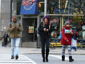 Pedestrians walk, against a light, on their phones, and outside of the crosswalk, across Bloor St. in Toronto on November 3, 2017. Dave Abel/Toronto Sun