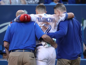 Troy Tulowitzki of the Toronto Blue Jays is helped off the field by trainers George Poulis and Mike Frostad after injuring his ankle on July 28, 2017. (TOM SZCZERBOWSKI/Getty Images files)