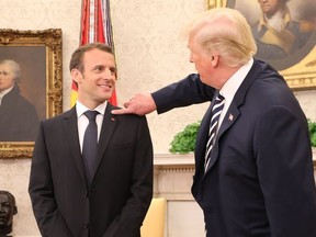 US President Donald Trump (R) clears dandruff off French President Emmanuel Macron's jacket in the Oval Office prior to a meeting at the White House in Washington, DC, on April 24, 2018.