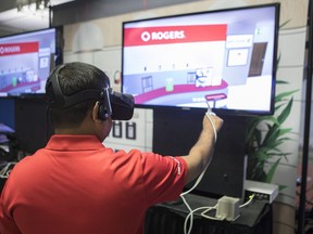 A Rogers employee wears VR goggles as he stands at a stall promoting VR retail over 5g, at a press event in Toronto on Monday, April 16, 2018, as Rogers Communications announced that it expects to test new high-speed 5G wireless networks in selected cities across Canada next year. THE CANADIAN PRESS/Chris Young