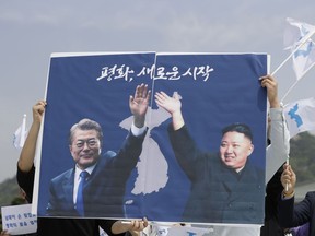 South Koreans hold a banner showing the pictures of South Korean President Moon Jae-in, left, and North Korean leader Kim Jong Un to welcome the planned summit between South and North Koreas near the presidential Blue House in Seoul, South Korea, Thursday, April 26, 2018. Seoul says North Korean leader Kim Jong Un and South Korean President Moon-Jae-in will plant a tree together and inspect an honor guard after Kim walks across the border for the leaders' historic summit. The letters read " Peace, A New Start."