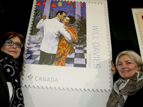 Pam Davies (L) and her sister Kerry stands next to a commemorative stamp showing a cover created for a Harlequin book illustrated by her father Will Davies on Friday April 6, 2018. Canada Post honours Will Davies as one of five Canadian illustrators featured on their latest stamps.