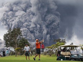 People play golf as an ash plume rises in the distance from the Kilauea volcano on Hawaii's Big Island on May 15, 2018 in Hawaii Volcanoes National Park, Hawaii. (Mario Tama/Getty Images)