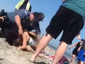 In a video posted online, a police officer can be seen punching a woman in the head at a beach in southern New Jersey. (NJ.com/YouTube)