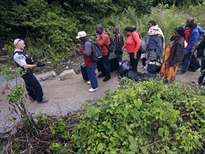 A RCMP officer, left, standing in Saint-Bernard-de-Lacolle, Quebec, advises migrants that they are about to illegally cross from Champlain, N.Y., and will be arrested, on Aug. 7, 2017.