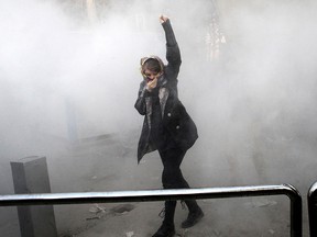 In this Saturday, Dec. 30, 2017 file photo taken by an individual not employed by the Associated Press and obtained by the AP outside Iran, a university student attends a protest inside Tehran University while a smoke grenade is thrown by anti-riot Iranian police, in Tehran, Iran.