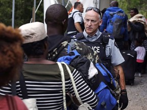 An RCMP officer standing in Saint-Bernard-de-Lacolle, Que., advises migrants that they are about to illegally cross from Champlain, N.Y., and will be arrested, Monday, Aug. 7, 2017.