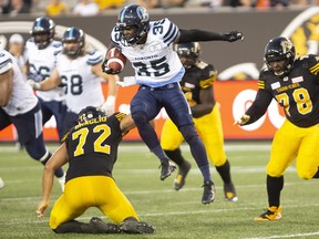 Argos’ Brandon Burks leaps over Tiger-Cats defensive end Roman Braglio as part of his spectacular 27-yard TD run off a screen pass during the first half of Friday’s pre-season game in Hamilton. Braglio was hurt on the play.  Peter Power/THE CANADIAN PRESS