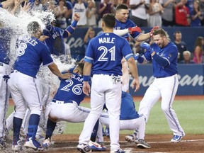 Justin Smoak (right) of the Blue Jays is greeted at home plate by teammates after hitting a game-winning solo home run in the bottom of the ninth inning against the Tigers at Rogers Centre in Toronto on Saturday, June 30, 2018.