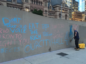 A city worker scrubbs angry messages scrawled on a wall at City Hall after Ontario Premier Doug Ford announced plans to cut City Council from 47 to 25 councillors on Friday, July 17, 2018. (Joe Warmington/Toronto Sun/Postmedia Network)