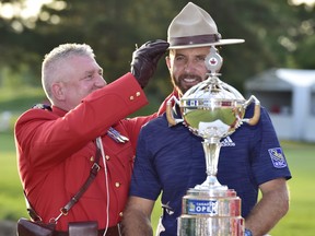 A Royal Canadian Mounted Police officer places an RCMP Stetson on Dustin Johnson as he poses with the Canadian Open championship trophy at the Glen Abbey Golf Club in Oakville Ont., on Sunday, July 29, 2018. THE CANADIAN PRESS/Frank Gunn