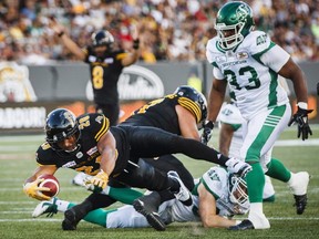 Tiger-Cats' John White IV, left, scores a touchdown past Roughriders' Jerome Messam, right, during first half CFL action in Hamilton, Ont., Thursday, July 19, 2018.