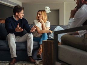 Couple arguing during therapy session with psychologist. Man and woman sitting on couch and talking while psychologist listening them. For a story by Clare Clancy