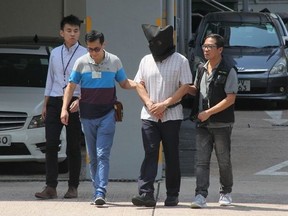 This handout photograph from Apple Daily taken on September 11, 2017 shows Malaysian national Khaw Kim-sun (C), who is accused of murdering his wife and daughter, being escorted by police at Ma On Shan Police Station in Hong Kong. - Khaw Kim-sun, an anaesthetist, gassed his wife and daughter to death using a yoga ball filled with carbon monoxide, a Hong Kong court has heard. Prosecutors told the High Court that Khaw Kim-sun left the inflatable ball in the boot of a car where the gas leaked out and killed them, according to reports from court on August 22, 2018.