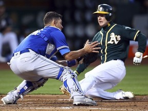 Toronto Blue Jays catcher Luke Maile, left, waits for the ball as Oakland Athletics' Mark Canha steals home plate in the third inning of a baseball game Tuesday, July 31, 2018, in Oakland, Calif.