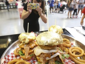 Toronto Sun reporter Jenny Yuen checks out a platter of $25 and $100 24-karat golden foil burgers at Bacon Nation in the food building as the 140th edition of the CNE opened on Friday August 17, 2018. (Jack Boland/Toronto Sun/Postmedia Network)