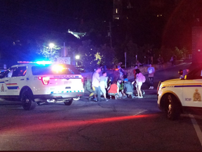 An officer attends to an injured person as a crowd looks on at the corner of Bank and Vittoria streets in front of Parliament Hill on Aug. 11, 2018. Social media photo.